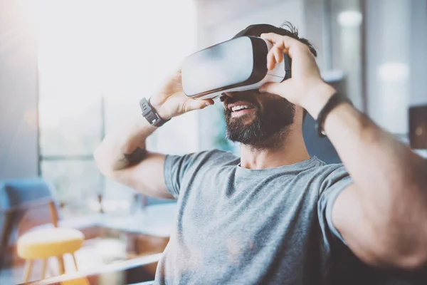 Bearded young man wearing virtual reality goggles in modern coworking studio. Smartphone using with VR headset in office. Horizontal, blurred. — Stock Photo, Image