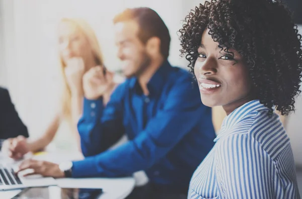 Portret van vrij Afro-Amerikaanse zakenvrouw met afro glimlachend in de camera. Coworking team in het proces op de achtergrond in moderne kantoor brainstormen. Horizontale, wazig. — Stockfoto