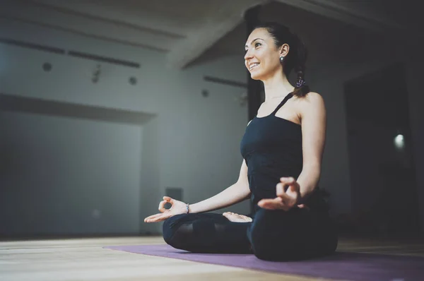 Retrato de una joven feliz practicando yoga en interiores. Hermosa chica practicar la posición de loto en class.Calmness y relajarse, felicidad femenina.Horizontal, fondo borroso, bengalas . —  Fotos de Stock