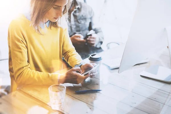 Jonge team van collega's samen gebruiken van mobiele apparaten in de moderne naaiatelier ruimte. Mooi meisje bericht te sturen met de smartphone. Horizontaal. Onscherpe achtergrond. — Stockfoto