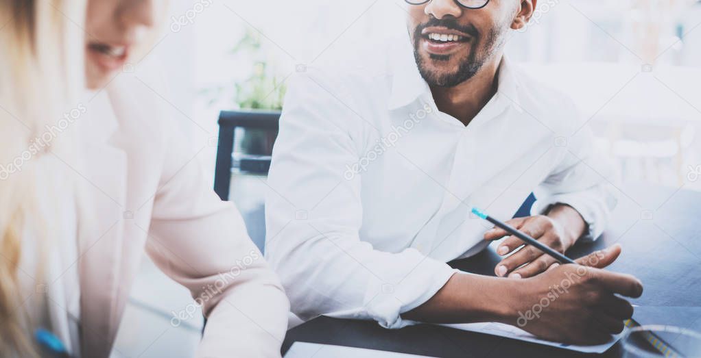 Two young coworkers working together in modern business project.Man smiling and wearing glasses, making work notes at the table.Horizontal,blurred background