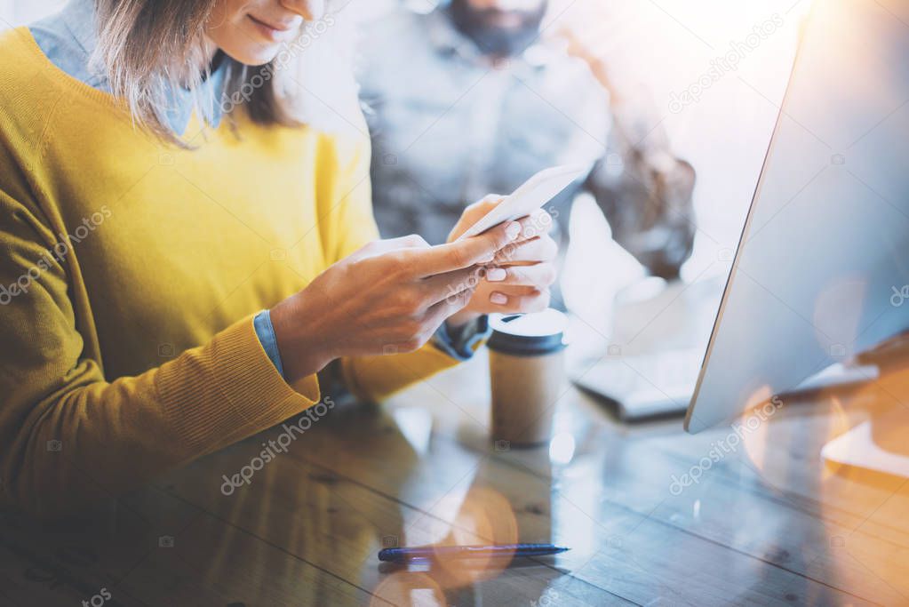 Young team of coworkers working together in modern coworking space.Woman sending message with smartphone. Man work on desktop computer.Horizontal,flare effect. Blurred background.