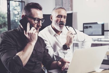 İş adamları işlem beyin fırtınası kavramı. Cep telefonu ve laptop için bul büyük iş çözüm isteyen yetişkin meslektaşım kullanan sakallı genç adam. Yatay, bulanık arka plan.