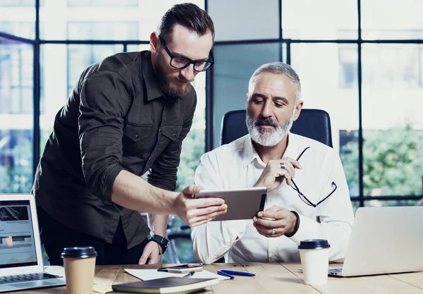 Концепция коворкинга людей. Молодой бородатый мужчина показывает стартап-идею на мобильном столе.Взрослый бизнесмен, работающий вместе за деревянным столом с партнером. — стоковое фото