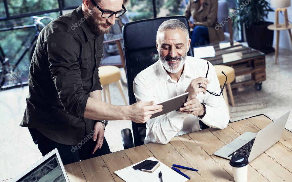Group of two coworkers making great time brake during work process in modern office.Adult bearded man watching mobile tablet and smiling.Business people meeting concept.Horizontal, blurred.