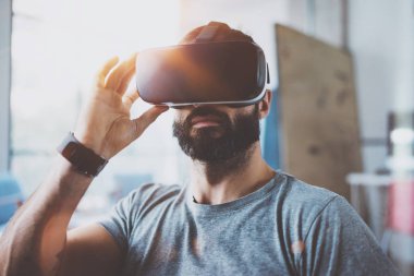 Sanal gerçeklik giyen sakallı adam modern iç tasarım stüdyo coworking gözlük. VR mezartaşı ile kullanılarak akıllı telefon. Yatay, fişekleri etkisi, arka plan bulanık.