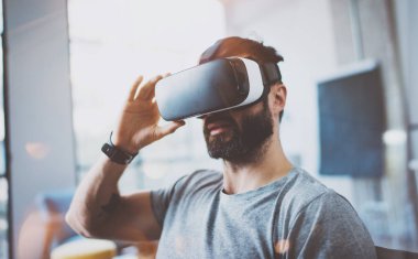 Sanal gerçeklik giyen çekici sakallı adam modern iç tasarım stüdyo coworking gözlük. Vr ile Smartphone kullanarak kulaklık gözlükler. Yatay, fişekleri etkisi, arka plan bulanık.