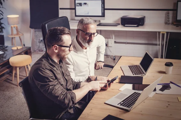 Conceito de pessoas de negócios processo de trabalho em equipe. Homem barbudo mostrando ideia de inicialização no telefone móvel. Homem de negócios adulto trabalhando em conjunto com o jovem parceiro na mesa de madeira. . — Fotografia de Stock