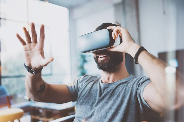 Young bearded man wearing virtual reality glasses in modern interior design coworking studio. Smartphone using with VR goggles headset. Horizontal,flares effect, blurred background. — Stock Photo, Image
