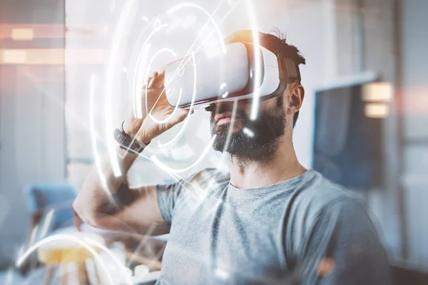 Begreppet digital skärm, anslutning och gränssnitt. Unga beraded hipster enjoyingvirtual reality glasögon i modern design loft studio. Smartphone användning med Vr glasögon headset. Soligt, flare effekt suddig — Stockfoto