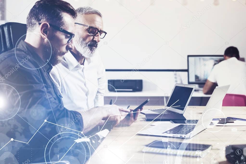 Concept of digital screen,virtual connection icon,diagram,graph interfaces.Bearded young man holding mobile phone and touching display.Adult businessman working together with partner.Film effect,flare