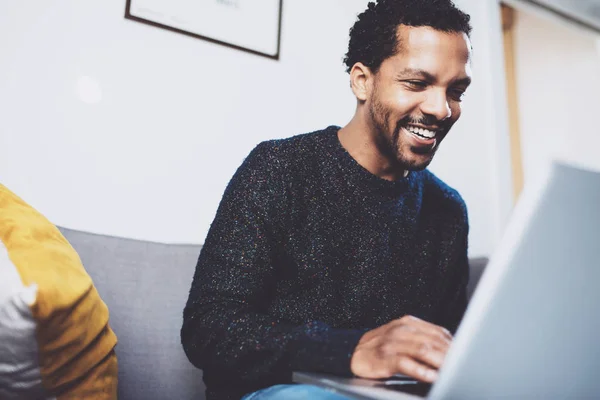 Mladí africké muž usmívající se a pomocí přenosného počítače sedí na jeho místě moderní coworkingu. Koncept šťastné lidi. Rozmazané pozadí. — Stock fotografie