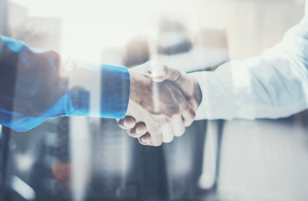 Double exposure concept.Close up view of business partnership handshake .Photo two businessman handshaking process.Skyscraper office building on the blurred background.Horizontal, film effect
.