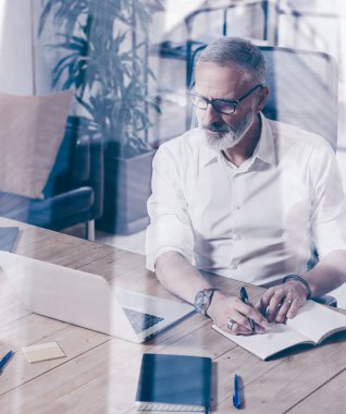 Klasik gözlüklü ve modern coworking yerde ahşap masa çalışan yetişkin başarılı işadamı kavramı. Çift pozlama, gökdelen ofis binası arka plan bulanık. Dikey.