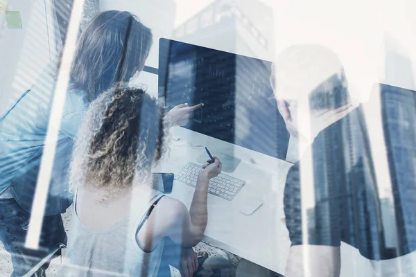 Groupe de jeunes travaillant sur ordinateur dans un studio de coworking moderne.Collaborateurs utilisant des gadgets électroniques.Icônes, graphiques et moniteur de diagramme.Double exposition, gratte-ciel, fond flou . — Photo