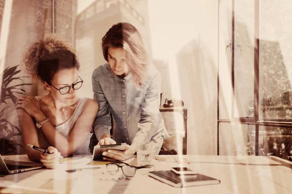 Jovens colegas de trabalho trabalhando no moderno loft.Two meninas usando tablet eletrônico no local de trabalho.Dupla exposição, arranha-céus edifício de escritórios desfocado background.Horizontal . — Fotografia de Stock