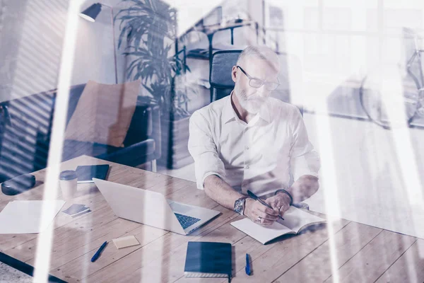 Konzept der erwachsenen stilvollen Geschäftsmann trägt eine klassische Brille und arbeitet am Holztisch in modernen Coworking-Platz.Doppelbelichtung, Wolkenkratzer Bürogebäude verschwommenen Hintergrund. — Stockfoto