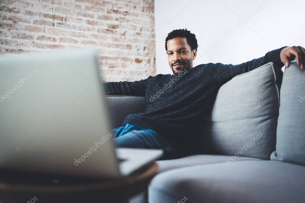 Young African man smiling and making video call via laptop while sitting at his modern home studio.Concept of happy business people.Blurred background.