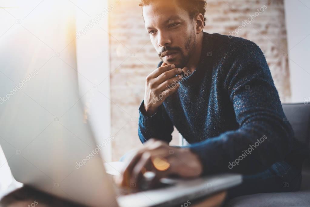 Young African man using laptop while sitting at his modern coworking place.Concept of business people full concentration.Blurred background, flares.