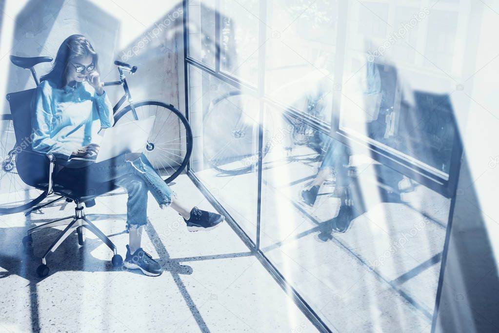 Beautiful young girl using modern laptop in design studio.Concept of coworking people work with computer.Double exposure,skyscraper office building blurred on background.Horizontal, film effect.
