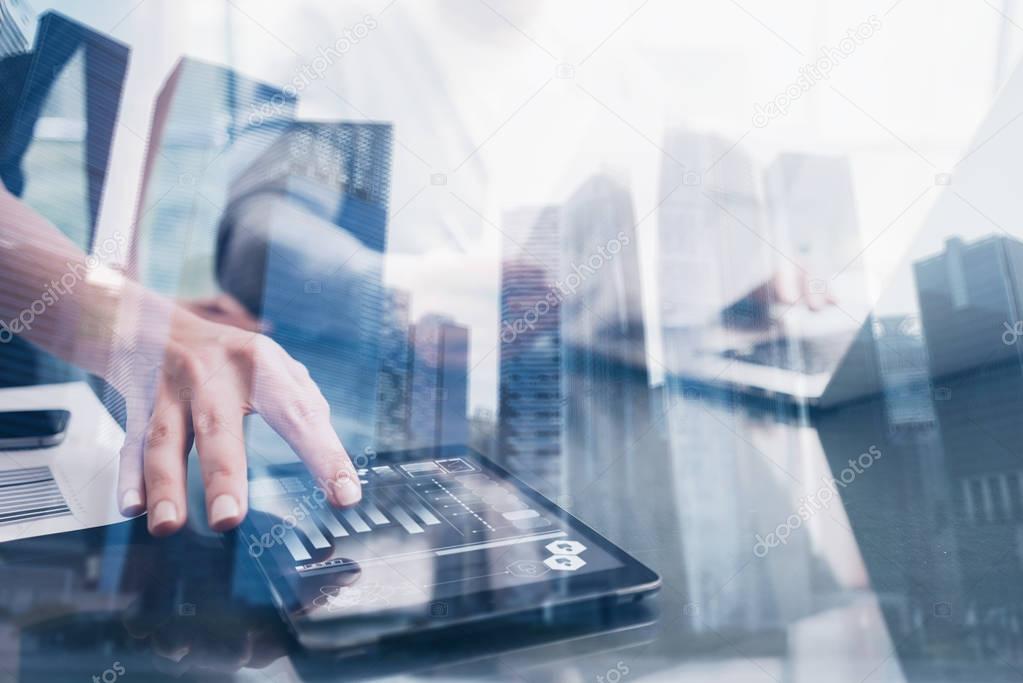 Closeup female hand touching tablet display in coworking place.Concept of business people using mobile divece.Icon and graphs on screen.Double exposure,skyscraper office building blurred background.