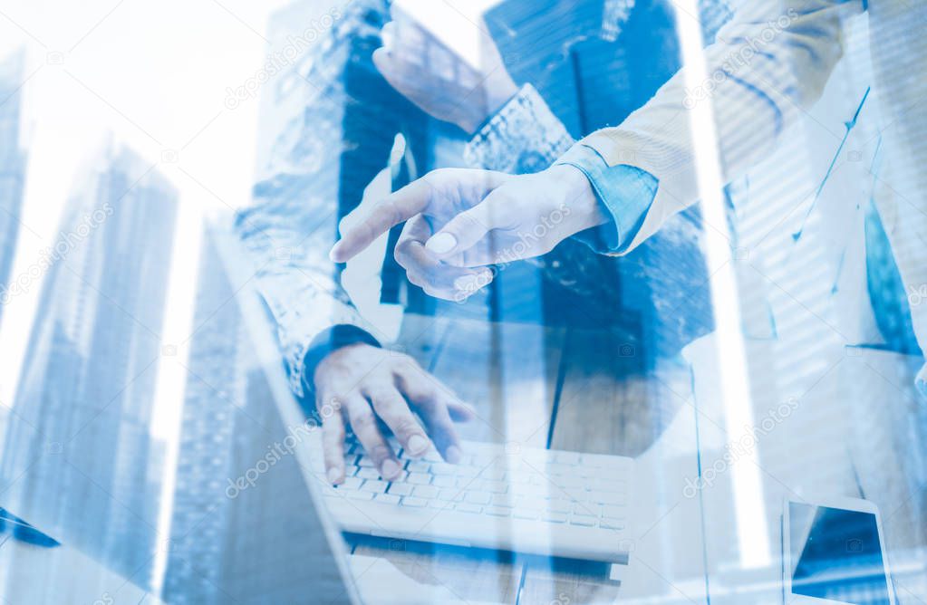 Double exposure concept.Businessman working in a coworking studio at the computer.Man using keyboard.Female hand pointing to desktop screen.Skyscraper office building blurred background.Horizontal.