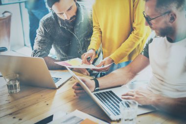 Güneşli bir ofis sürecinde coworking. Ahşap masa, bilgisayar üzerinde çalışan iki sakallı adamın. Sarı kazak ve gösteren belge onun elinde giyen kadın. Yatay, bulanık arka plan