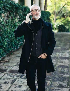 Onun Smartphone'da şehir parkında yürürken konuşmak başarılı orta yaş işadamı portresi. Dikey, bulanık arka plan, film etkisi.