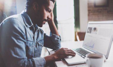 Evde vakit ise dizüstü bilgisayarda çalışan Afrika erkeğin sakallı. Mobil cihazlar kullanarak genç iş adamları kavramı. Bulanık bilgi defter perde. Seçici odak.