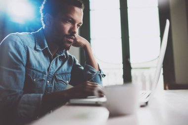 Bir güneşli sabah masada otururken pazarlama haber dizüstü okuma dalgın Afrika delikanlı. İnsanların çalışma ev coworking kavramı. Arka plan bulanık parlama efekti.