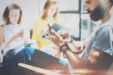 Sakallı hippi adam kanepede otururken modern smartphone kullanarak Partrait. Stüdyo ofisinde toplantıda grup arkadaşları. Yatay, bulanık arka plan, fişekleri.