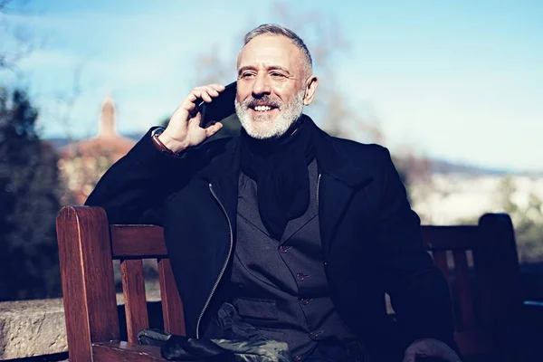 Retrato de empresário confiante feliz com seu smartphone enquanto sentado no parque da cidade.Horizontal, fundo embaçado . — Fotografia de Stock