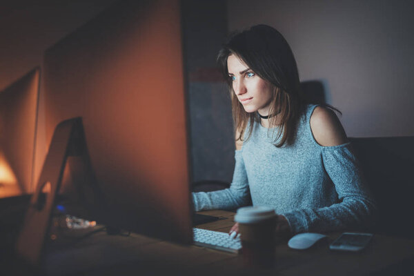 Молодая симпатичная женщина работает ночью в современном офисе студии. Девушка, использующая современный настольный компьютер, размытый фон. Горизонтальный, эффект пленки
.