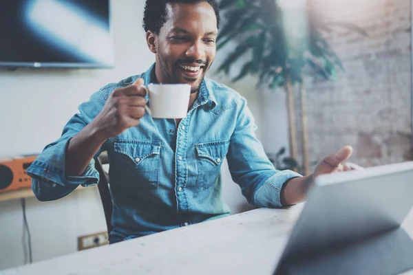 Afrika delikanlı güneşli ofiste siyah kahve içme sırasında video dijital tablet ile ortakları ile muhabbet gülümseyerek. Mutlu iş adamları kavramı. Arka plan bulanık film etkisi. — Stok fotoğraf