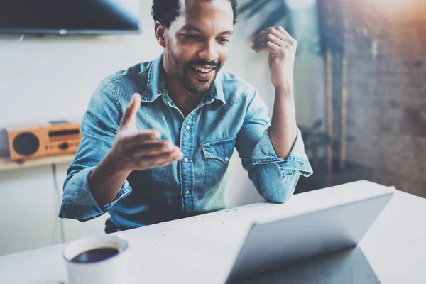 Sonriente joven africano hombre haciendo conversación de vídeo a través de tableta digital con socios de negocios mientras está sentado en la sala de reuniones soleada.Concepto de feliz coworking people.Blurred fondo, bengala . —  Fotos de Stock