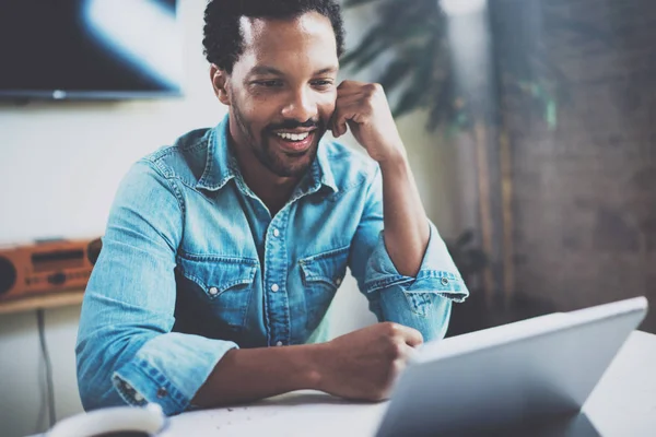 Güneşli toplantı odasında otururken video dijital tablet ile iş ortakları ile muhabbet çekici Afrika adam gülümsüyor. Mutlu coworking insanlar kavramı. Arka plan bulanık.