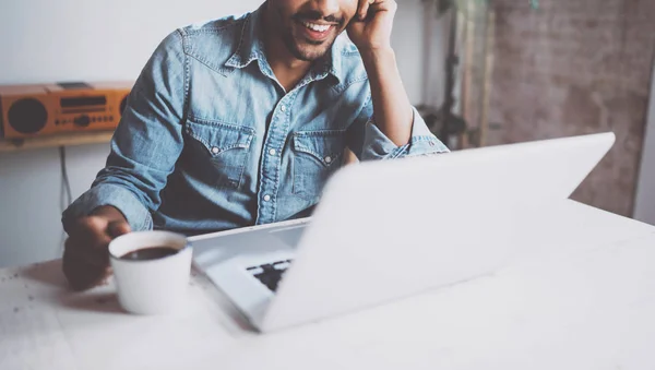 Hombre africano barbudo feliz haciendo conversación de vídeo a través de un ordenador portátil moderno con los socios, mientras que la celebración de la taza blanca de café negro en casa.Concepto de la gente joven de negocios.Fondo borroso, cosecha . —  Fotos de Stock