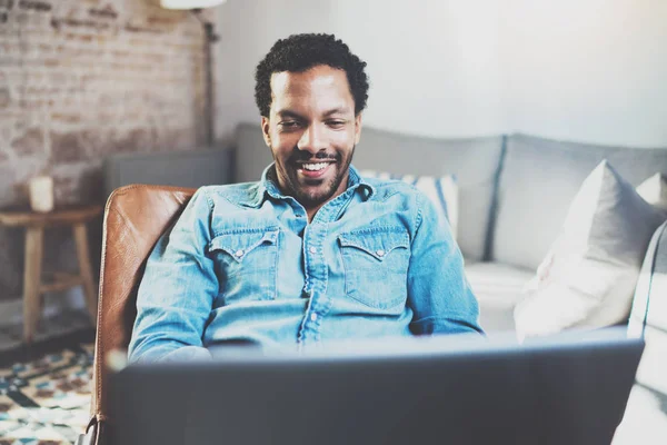 Attraktive bärtige afrikanische Mann mit Laptop beim Entspannen auf Sesseln in modernen Büro.Konzept der jungen Geschäftsleute, die zu Hause arbeiten.verschwommener Hintergrund.selektiver Fokus. — Stockfoto