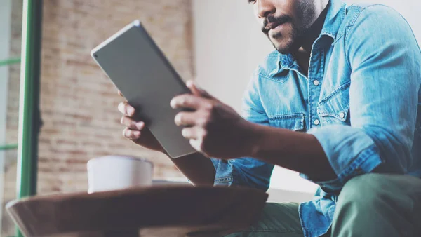 Homem Africano Pensivo usando tablet para conversa em vídeo enquanto relaxa no sofá no escritório moderno.Conceito de jovens empresários que trabalham em casa.Fundo borrado. Foco seletivo, colheita — Fotografia de Stock