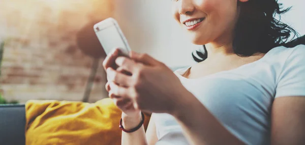 Close-up beeld van jonge lachende Aziatische vrouw zittend op de Bank thuis, het dragen van witte tshirt en typen handen op smartphone. Horizontaal wazig, fakkels effect. Wide.Selective focus. — Stockfoto