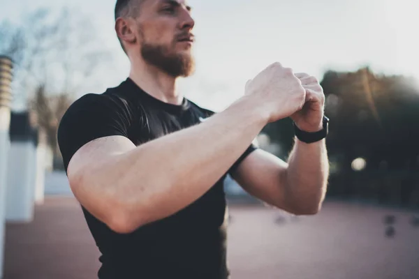 Concepção de estilo de vida.Jovem homem esticando os músculos do braço antes do treinamento.Atleta muscular se exercitando fora no parque ensolarado. Fundo desfocado . — Fotografia de Stock