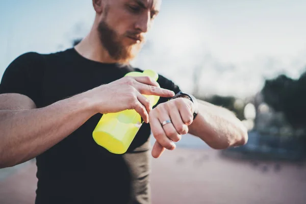 Gespierde bebaarde atleet controleren calorieverbruik op toepassing van de elektronische slimme horloge na goede training buiten sessie op stadspark. Onscherpe achtergrond. — Stockfoto