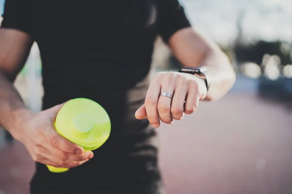 Muskulöser junger Athlet überprüft Herzfrequenz und Kalorien auf seiner Smartphone-Anwendung nach einer guten Trainingseinheit im Freien auf einem sonnigen Park.verschwommener Hintergrund. — Stockfoto