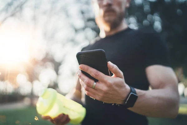 Muskulöser junger Athlet checkt nach gutem Training im Freien auf sonnigem Park.verschwommener Hintergrund. — Stockfoto