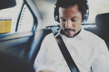 Pensive african man listening music on smartphone while sitting on backseat in taxi car.Concept of happy young people traveling.Blurred background. clipart