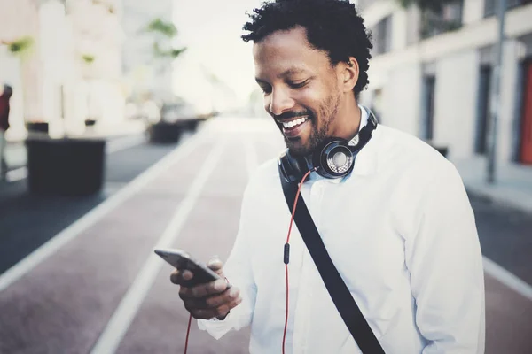 Feliz sonriente hombre africano utilizando el teléfono inteligente al aire libre.Retrato de joven hombre alegre negro mensajes de texto un mensaje de texto con los amigos.Fondo borroso . —  Fotos de Stock