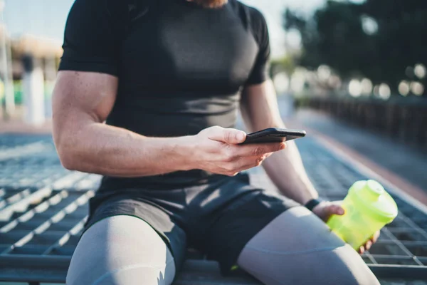 Atleta muscoloso bello controllare calorie bruciate su applicazione smartphone e smart watch dopo una buona sessione di allenamento sul parco cittadino nella soleggiata mattinata. . — Foto Stock