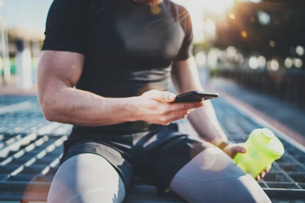 Atleta bonito muscular verificando calorias queimadas no aplicativo smartphone e relógio inteligente após uma boa sessão de treino no parque da cidade na manhã ensolarada.Fundo desfocado . — Fotografia de Stock