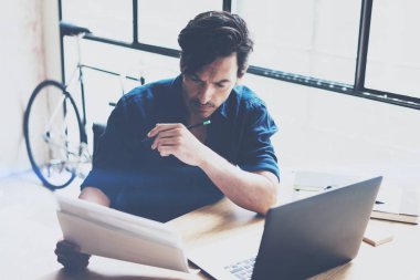 Ahşap masada otururken dizüstü bilgisayarda güneşli iş yerinde çalışan genç iş adamı. Adam belge bilgisayar notebook üzerinde analiz. Arka plan bulanık. Yatay.