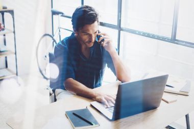 Modern çatı katında ahşap masada otururken çağdaş dizüstü çalışan İspanyol zarif bir iş adamı. Cep telefonundan konuşan adam. Arka plan bulanık. Yatay